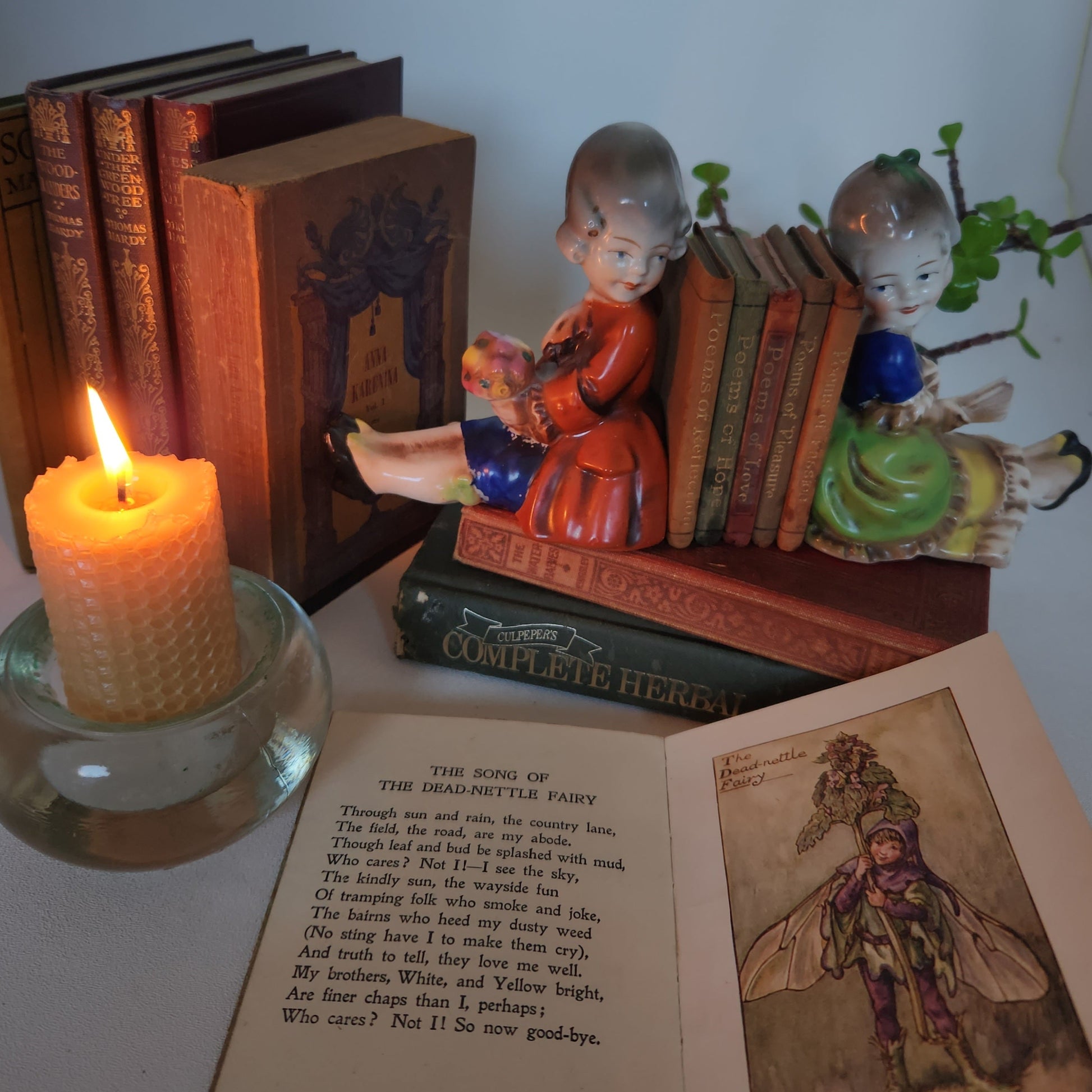 Decorative setup with books, figurines, and a lit candle on a surface.